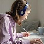 A middle school student taking notes and listening to an online class through headphones